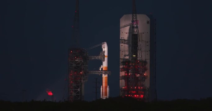 A space rocket sits on the launch pad at dusk as is prepares to launch a satellite into space.  No markings or logos visible.