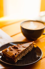 Cake with peanuts and caramel, cup of cappuccino.