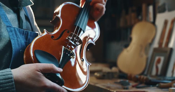 Slow motion close up of master artisan luthier controlling a quality of handmade violin  in a workshop. Shot in 8K.Concept of spiritual instrument, handmade, art, orchestra, artisan, passion for music