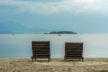Two wooden beach chairs in front of the sea.
