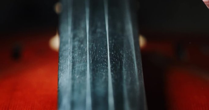Slow motion artistic macro of master artisan luthier playing with a bow on a handmade violin or cello. Shot in 8K. Concept of spiritual instrument, art, orchestra, passion for music, sound, precision