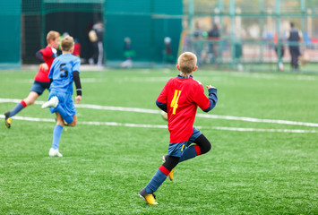 Obraz premium Boys in red white blue sportswear running on soccer field. Young footballers dribble and kick football ball in game. Training, active lifestyle, sport, children activity concept