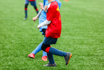 Naklejka premium Boys in red white blue sportswear running on soccer field. Young footballers dribble and kick football ball in game. Training, active lifestyle, sport, children activity concept