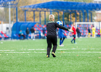 Goalkeeper kicks ball. Young footballers dribble and kick football ball in game. Boys in red  blue sportswear running on soccer field. Training, active lifestyle, sport, children activity concept