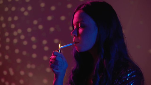 Serious young woman smoking cigarette at nightclub party, unhealthy habit