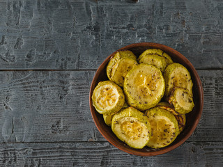A clay bowl filled with baked zucchini on a black wooden table. Vegetarian dish. Natural plant food. Flay lay.