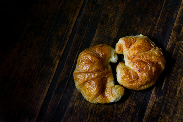 Freshly baked croissants in a black ceramic plate on the dark wooden background. Baking/pastry background. Concept for croissants making. Free space for text,two croissants on dark wood table