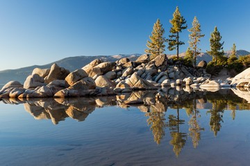 Beautiful Lake Tahoe along the shoreline at golden hour sunset with boulder rocks poking out of the blue water
