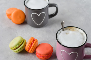 pink and gray cups with cappuccino and macaroons (macaron). cups painted hearts, gray background. romantic breakfast.