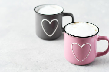 pink and gray cups with cappuccino. cups with  hearts, gray background. concept of romantic love, romantic breakfast, concept of romantic couple.  selective focus and copy space 