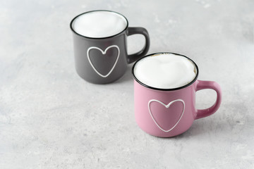 pink and gray cups with cappuccino. cups with  hearts, gray background. concept of romantic love, romantic breakfast, concept of romantic couple.  selective focus and copy space 
