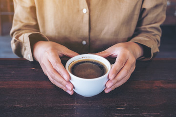 Closeup image of woman's hands holding a cup of hot coffee on wooden table