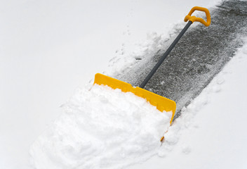 close up on snow shovel removing snow on the driveway