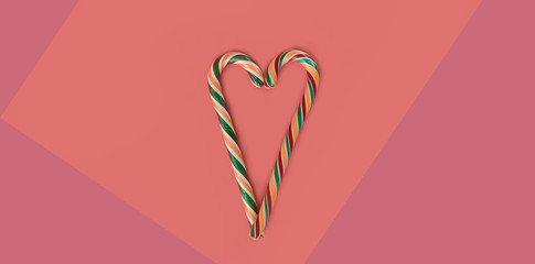 two striped candy stick in the shape of a heart, coral background. love concept, minimalism, food Flat lay, copy space for text