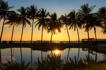 Obraz premium Warm tone, Swimming pool with Silhouette coconut tree and sea background, reflection of coconut trees on the swimming pool at the beach, Sunset in Tropical island at Andaman sea, Ranong estuary,Thai
