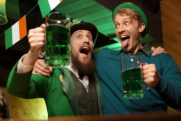 Dark-haired bearded young man in a leprechaun hat and his friend looking drunk
