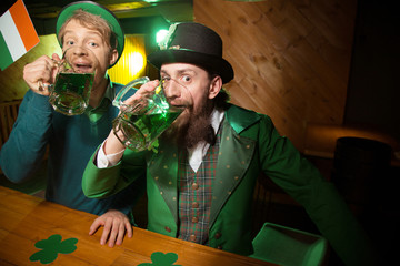 Fair-haired young man in a green hat and his bearded friend feeling silly