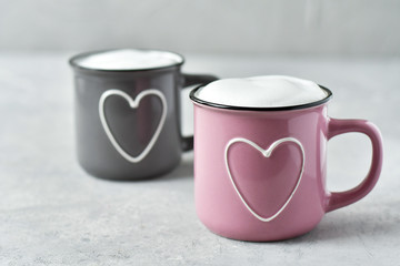 pink and gray cups with cappuccino. cups with  hearts, gray background. concept of romantic love, romantic breakfast, concept of romantic couple.  selective focus and copy space 