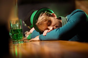 Fair-haired young handsome man in a green hat sleeping at the bar counter