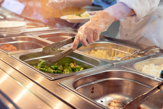 Chef standing behind full lunch service station with assortment of food in trays.