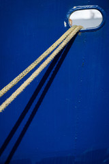 Mooring lines from a ship and their shadow against the blue hull of a ship