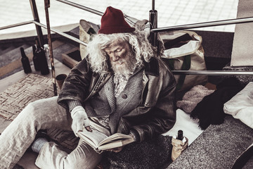 Homeless old man reading book he found with enthusiasm.