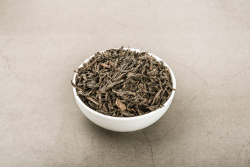 Dried tea is poured into a white ceramic cup on a gray textured background.