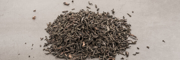 Dried tea is poured scattered on a grey textured background.