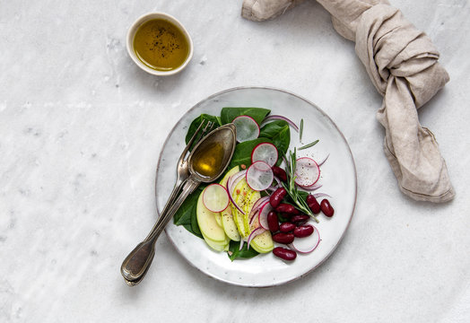 vegetarian salad with radish, red beans, apple, spinach, rosemary and olive oil in rustic plate on marble background with copy space