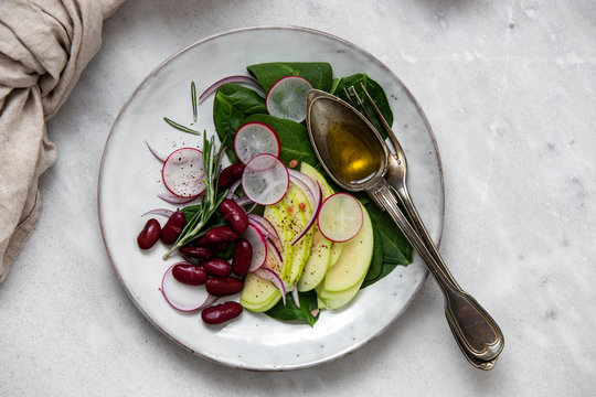 vegetarian salad with radish, red beans, apple, spinach, rosemary and olive oil in rustic plate on marble background with copy space