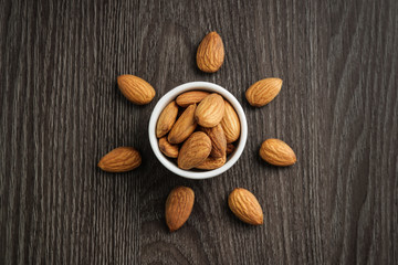 almonds in bowl and scattered on wooden background stylized sun shape top view flat lay 