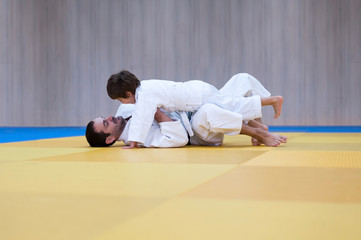 Young judo student and his father engaged in judo class in a dojo. Trainer teaches child the methods and positions of ground fighting in judo or brazilian jujutsu