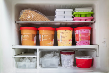 Full of bucket container ice creams flavors and ice cubes in freezer get ready for summer. - obrazy, fototapety, plakaty