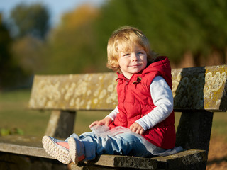 Little girl with red vest sitting on bench