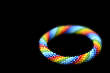 Kid's roll-on rainbow bracelet made of seed beads isolated on a black background close up