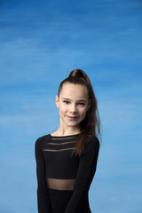 Portrait of a beautiful little brown-haired girl smiling on a blue background. Dressed in a black sweater, hair collected in a ponytail.	