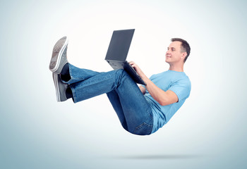 Relaxed man in casual clothes working on a laptop soaring in the air. Unreal concept comfort