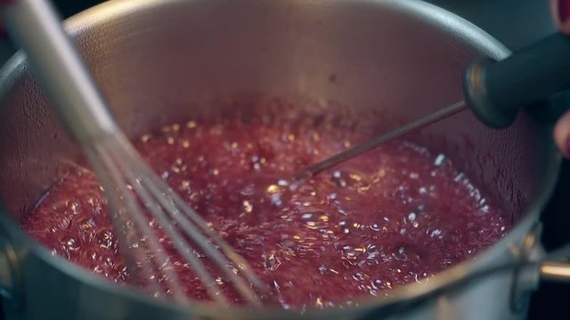 close view confectioner with purple manicure boils sweet red caramel in metal saucepan and regulates temperature