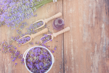 Top view of a bowl and wooden spoons with fresh lavender flowers, lavender essential oil and a bouquet of lavender on a brown wooden background.