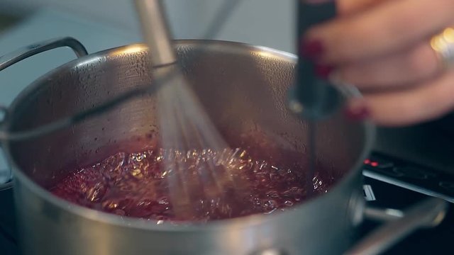 closeup woman finishes boiling sweet red berry caramel and regulates temperature using cooking thermometer
