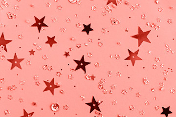 Delicate glitter star confetti on coral background. Creative and moody color of the picture.