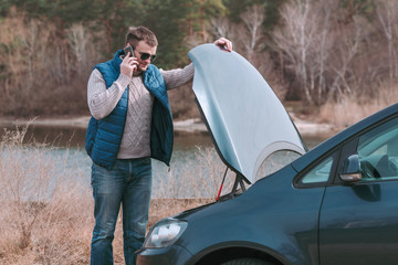 Young handsome man having problem with car and calling for help.