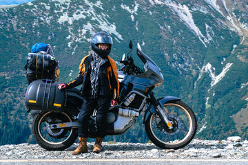 Woman biker and adveture motorcycle top mountain road. Travel, vacation in Europe, motorcyclist way, tourism, Transalpina, Romania. copy space, motorcyclist outfit, body, arm, leg, helmet protection