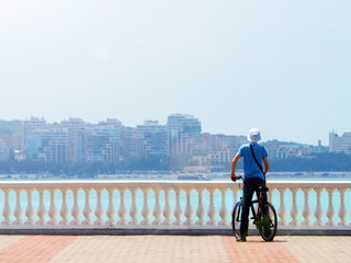 Cyclist on the promenade admiring the view of the city, sunlight. Man cycling looking at the sea