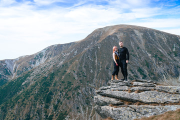 A young couple in love, standing on a stone on a mountaintop, a victory concept, conquering mountains, adventures and traveling on a motorcycle on the Transalpina road, Romania