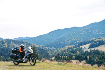 Woman biker with big adventure motorbike, motorcyclists vacation, world traveler, long road trip on two wheels. autumn day. Mountains on background. Romania