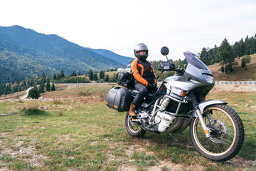 Woman biker with big adventure motorbike, motorcyclists vacation, world traveler, long road trip on two wheels. autumn day. Mountains on background. Romania