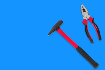 Metal hammer and pliers with black and red rubber handle on blue table in workroom. Top view. Repair or building concept. Copy space for your text