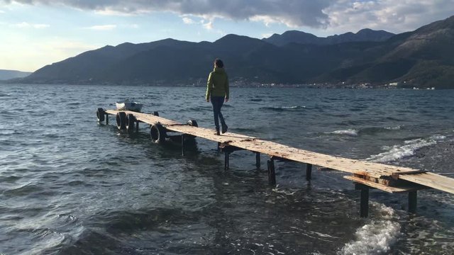 Girl is walking on the olde wooden pier and watching on a sunset over sea 