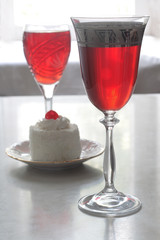A glass of red wine and a cake with cherry and white cream
